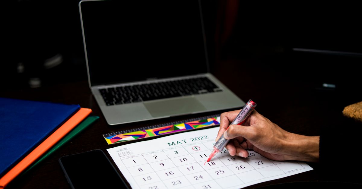 Hand marking a date on a wall calendar with a pen