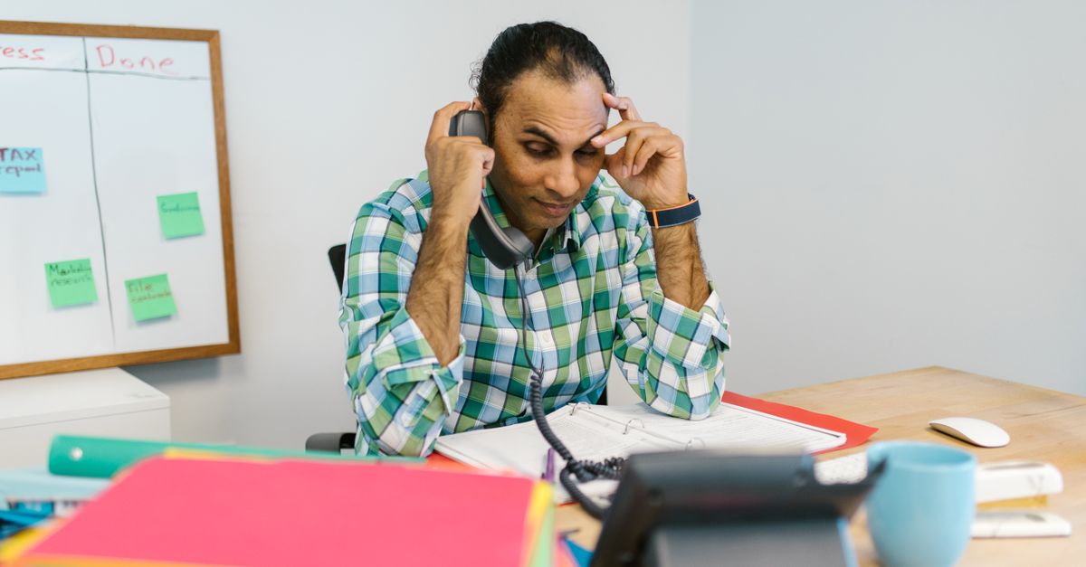 Stressed small business owner surrounded by work and a ringing phone
